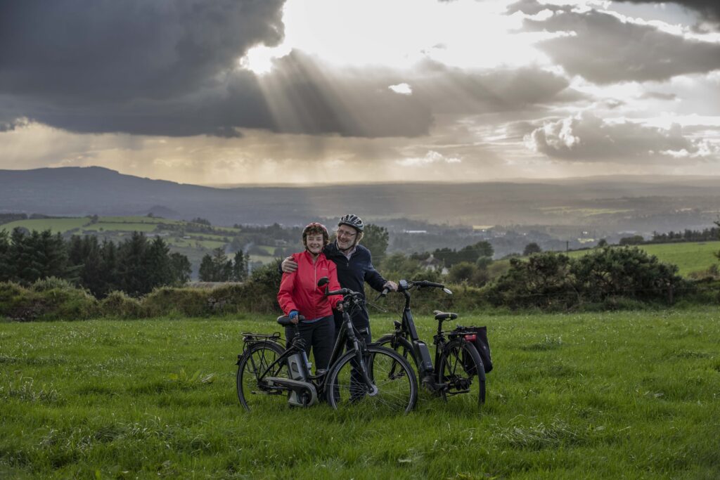 Paddy and Anna Lane of Mallow, Co. Cork in a field embracing each other and standing with their electric bicycles.
