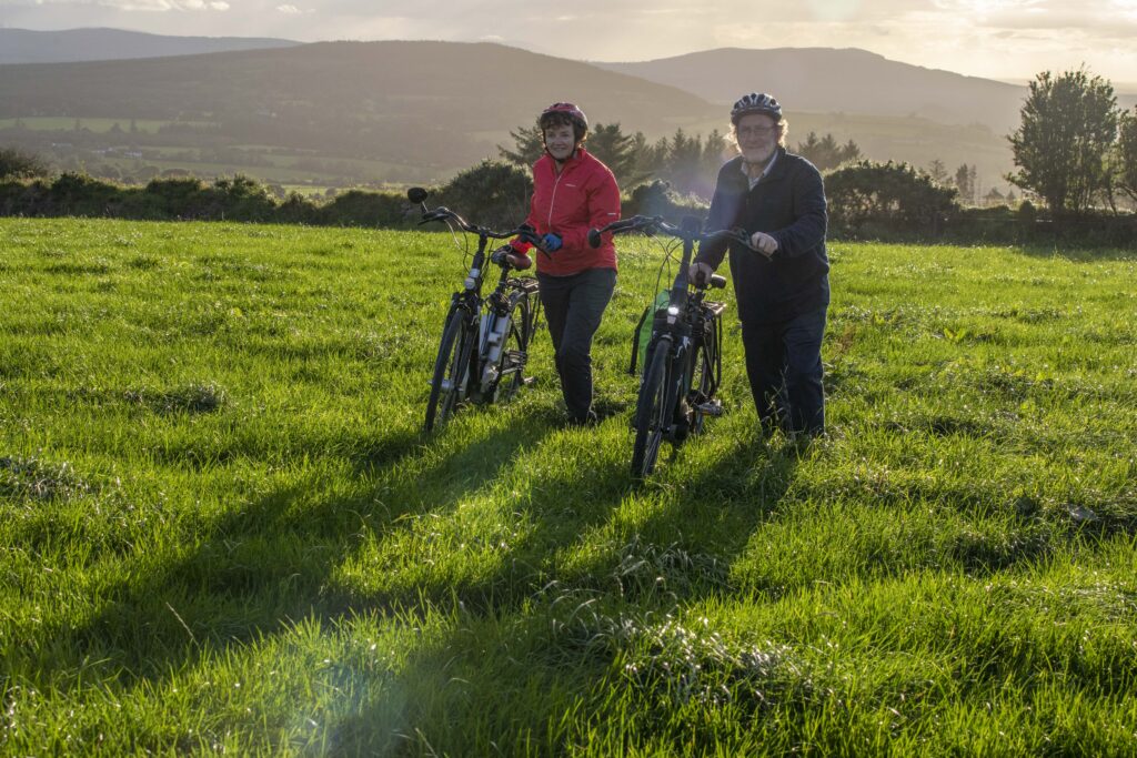 Paddy and Anna Lane of Mallow, Co. Cork walking with their electric bicycles in a field.